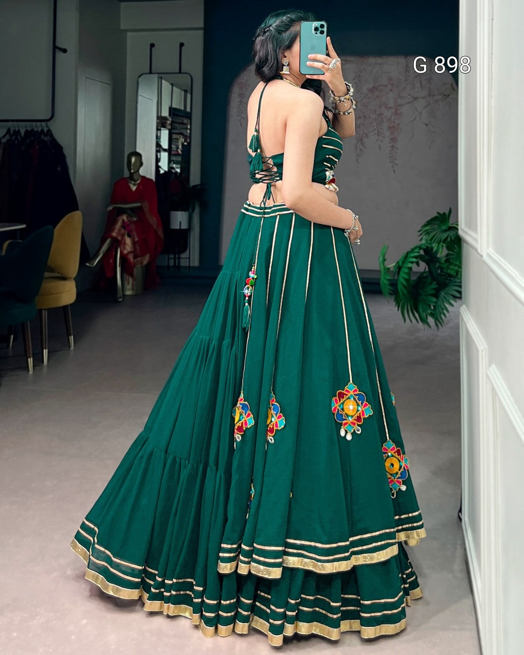 Woman wearing a green embroidered traditional outfit taking a mirror selfie.