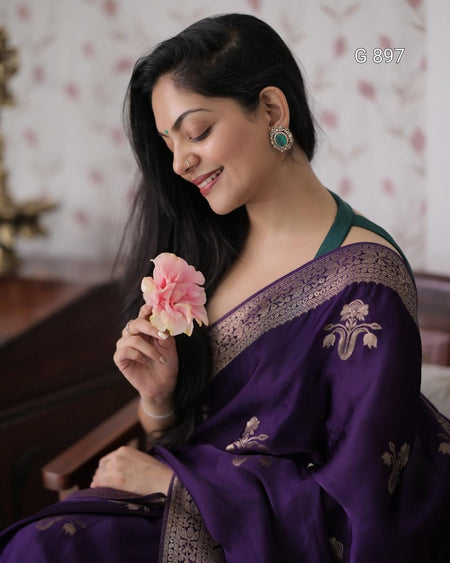 Woman in a purple saree holding a pink flower indoors.