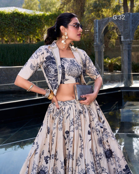 A woman models a beige and navy floral printed traditional outfit consisting of a kurta, cropped blouse, and flared skirt, styled with gold jewelry and sunglasses in an outdoor setting.