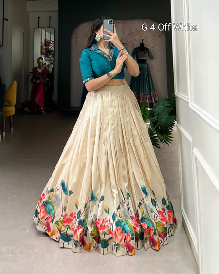 A woman takes a mirror selfie in a boutique wearing a traditional Indian outfit consisting of a teal green embroidered blouse and a voluminous off-white skirt with a colorful floral border. The text 'G 4 Off White' is visible in the top right corner.