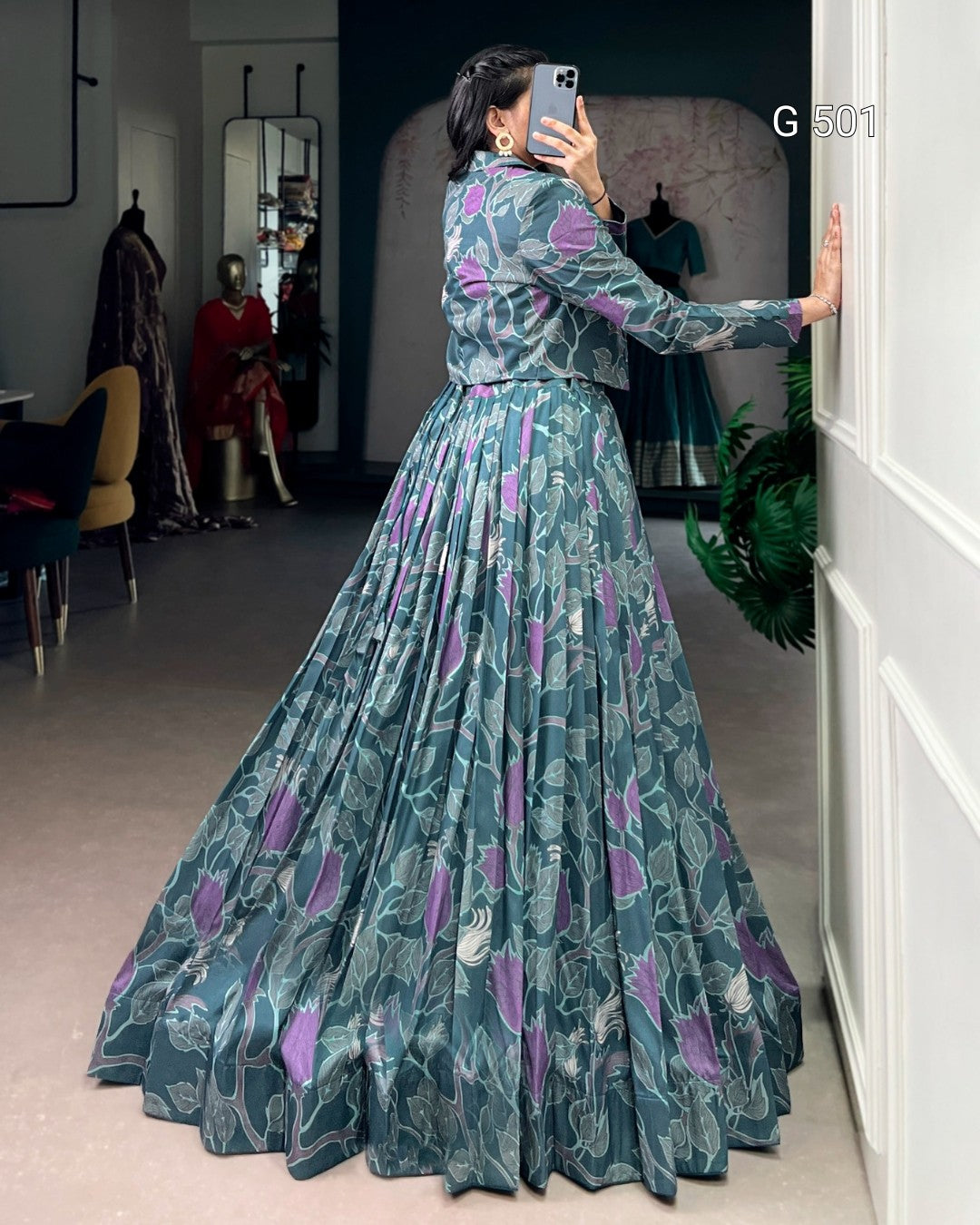 Woman taking a mirror selfie wearing a long, floral-patterned dress in a room.
