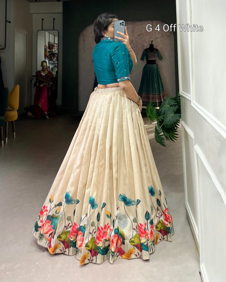 A woman takes a mirror selfie in a boutique wearing a traditional Indian outfit consisting of a teal blue blouse and a voluminous off-white skirt with colorful floral patterns at the hem. Text overlay reads 'G 4 Off White'.